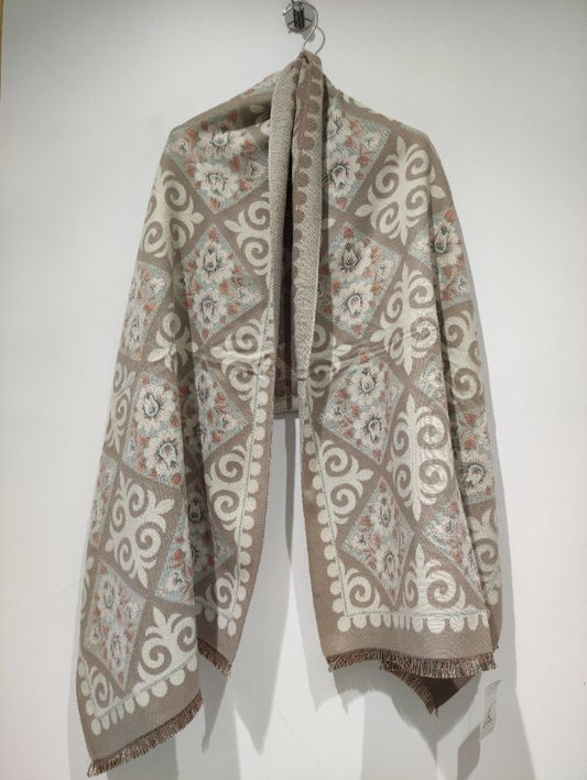 Gros plan sur le châle jacquard Pomelo de couleur taupe suspendu, montrant les motifs détaillés de losanges fleuris et les franges soignées.